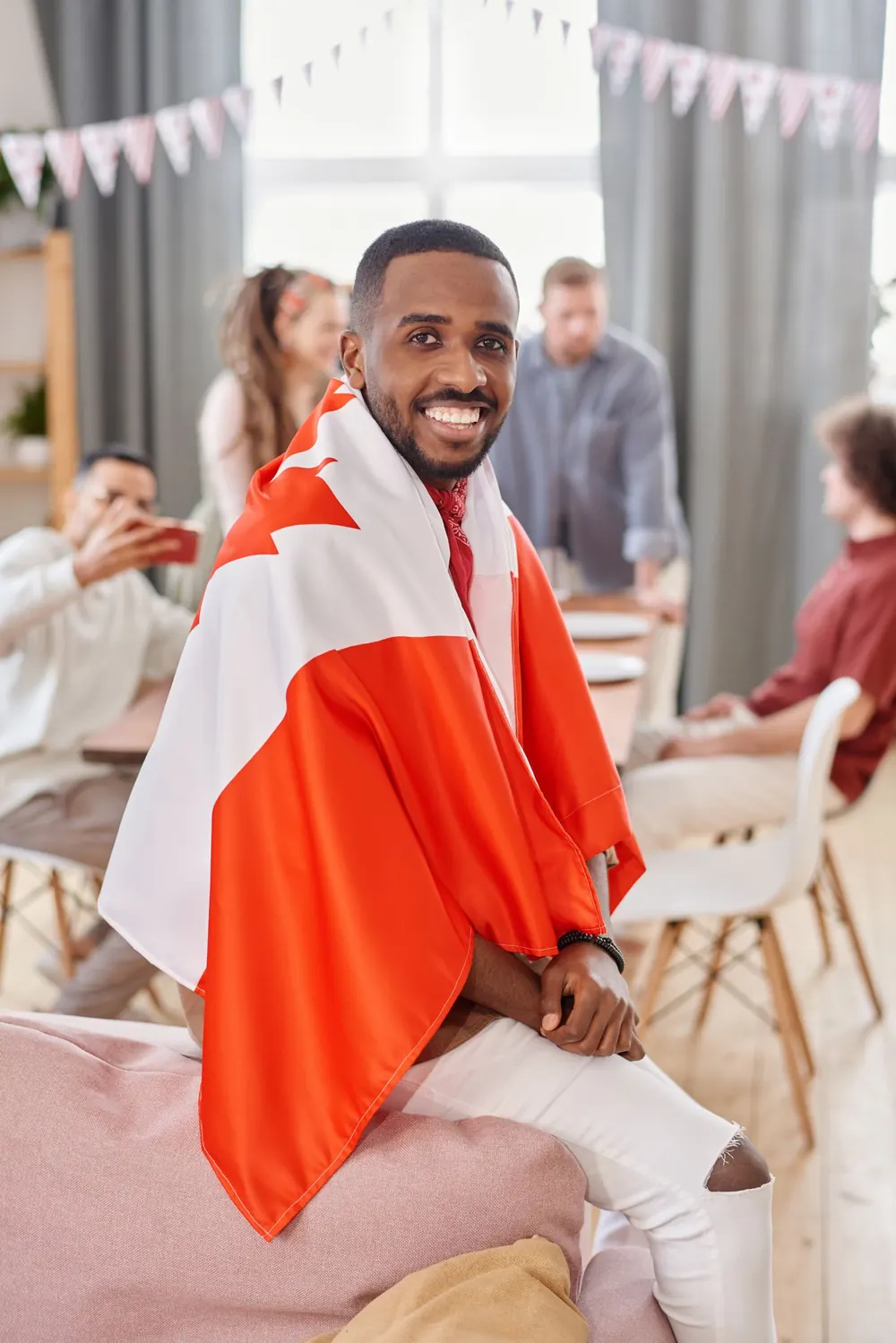 A smiling Black man wearing the Canadian flag as a cape